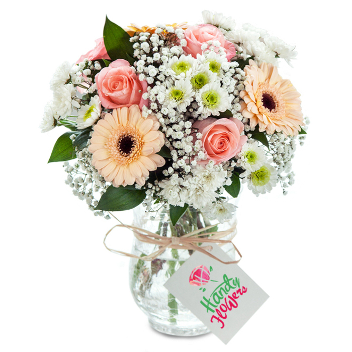 A vision of soft elegance, this expertly arranged bouquet is inspired by Battersea's riverside colors and creative heart. Centered in the composition are plush peach-pink roses, their gently spiraling petals creating a sense of unfolding romance and optimism. Framing them, two bold peachy gerberas stand upright, their vibrant, open petals and pronounced brown centers echoing the cheerful vibrancy of Battersea's weekend flower markets. Accents of baby's breath float throughout-each blossom like a whisper of cloud over Wandsworth Common-layering the bouquet with lightness and texture. Mingling with these, neat white spray chrysanthemums with almost lime-green eyes bring rhythm and modernity, reflecting the fresh buzz of St. John's Hill. Traces of deep eucalyptus foliage add richness and a hint of woodland scent, balancing the pastels' lightness. Presented in a textured clear glass vase, the arrangement's stems and pure water are revealed, exuding freshness and authentic craftsmanship. Encircling the vase neck, a rustic band of twine suspends a small, white card, perfect for a note of encouragement or love. Expertly lit, the bouquet glimmers, inviting admiration in a Battersea kitchen or as a gift for celebrations in Queenstown Road. Every petal and detail express the artistic touch of local florists.